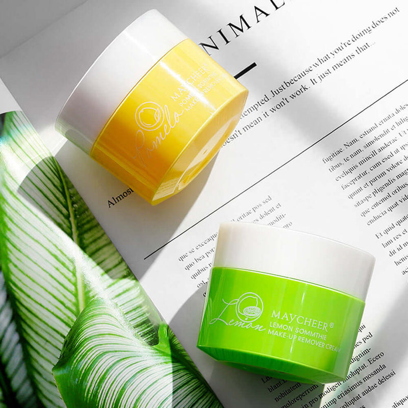 Meiqianer deep cleansing makeup remover cream jars in lemon and grapefruit, placed on a stylish magazine with green leaves.