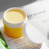 Open jar of Maycheer skincare product on a magazine page, showcasing its creamy texture and vibrant packaging.