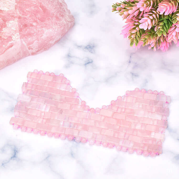 Pink crystal facial mask on a marble surface with flowers, highlighting beauty and relaxation.
