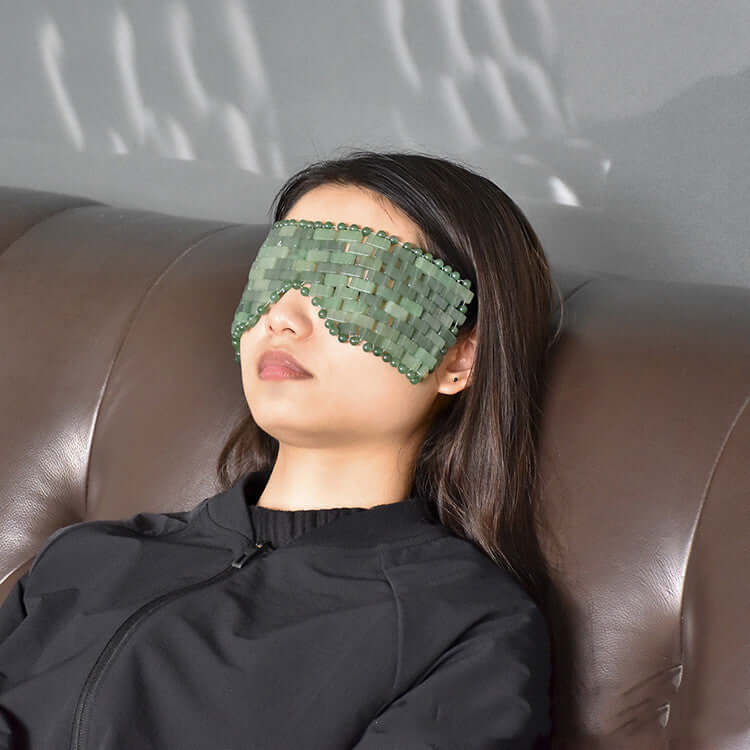 Relaxing woman wearing a green jade eye mask for facial lifting and massage benefits.